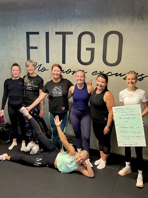 Medlemmer av FITGO som deltar på arrangementet Breakfast Club og som har stilt seg foran veggen med FITGO logoen og smiler og er glade etter økta