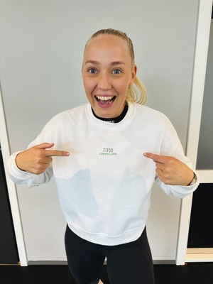 Personlig trener i løpeklubben som peker på FITGO logoen på genseren sin og smiler bredt